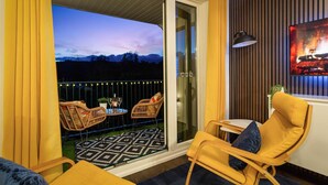 A balcony with wicker chairs, a small table with drinks, and a view of mountains at dusk. - Rigg & Rest - Central Bowness, Balcony & Parking (Bowness-on-Windermere)