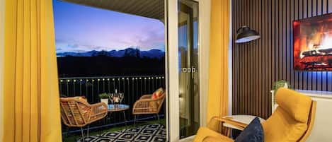 Un balcon avec des fauteuils en osier, une petite table avec des boissons et une vue sur les montagnes au crépuscule.
