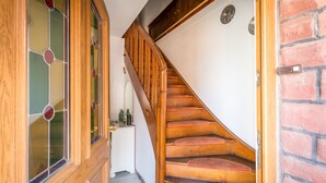 Una escalera de madera con barandilla, una pared blanca y una pared de ladrillo.