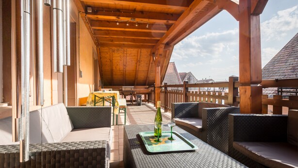 Un patio al aire libre con mobiliario de mimbre, una mesa de vidrio con una botella y un vaso, y una estructura de pérgola de madera.