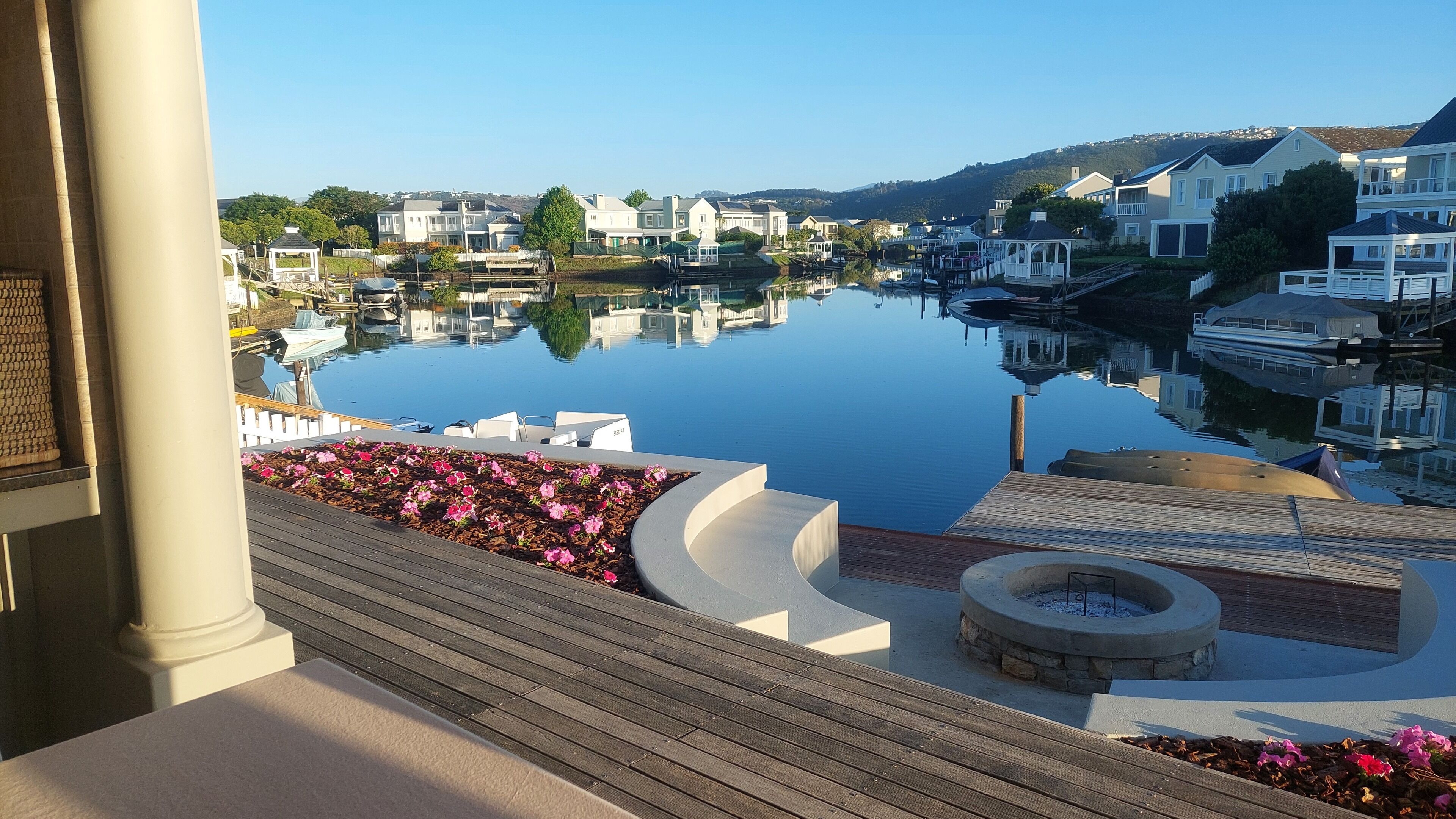 A waterfront view with a calm lake, a wooden deck, and a stone fire pit.
