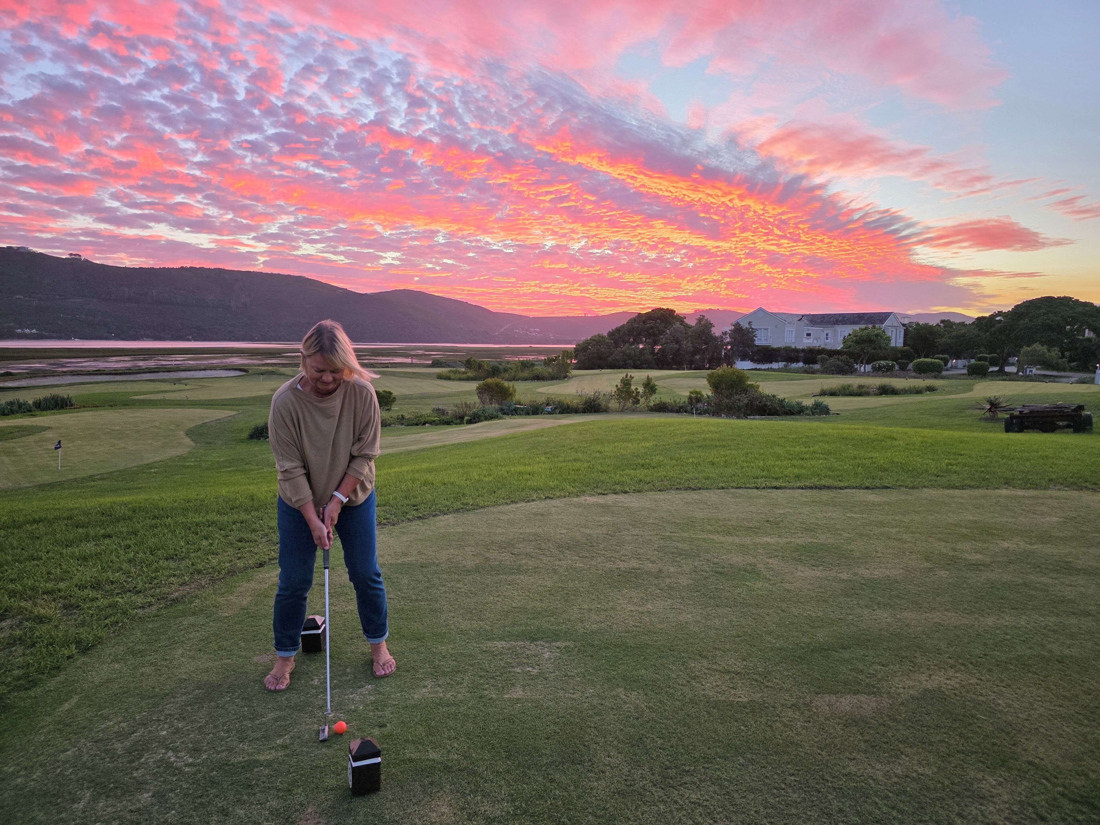 A person playing golf on a well-maintained course with a scenic sunset view in the background.