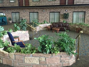 Une cour avec un mur en briques, un canapé en cuir marron, une chaise bleue et des plantes en pot.