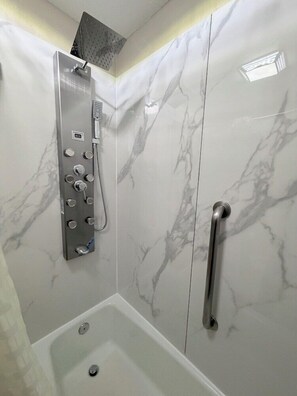Ein modernes Badezimmer mit Dusche, einer Handstange und einer Marmorwand.