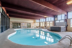 Una piscina interna con vasca idromassaggio, poltrone relax e un muro in mattoni.