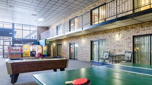 Une table de billard avec une queue de billard et une table de ping-pong, dans un bâtiment aux murs en briques et aux grandes fenêtres.