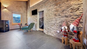 A modern interior with stone walls, a wooden ceiling, a television, a green chair, and two gnome figures. - Chalet 'Al Volt' with Mountain View, Private Terrace and Garden (Voiandes)