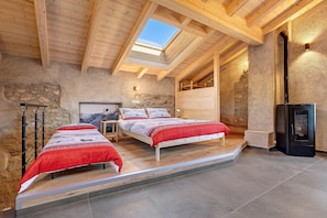 Une chambre avec deux lits, une lucarne, des murs en pierre et un poêle à bois.