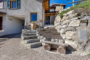 Un escalier en pierre menant à une porte en bois, un mur de pierre avec un nid, et une grille métallique.