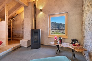 Un intérieur rustique avec un mur en pierre, une table en bois offrant une vue dégagée, une cheminée et une fenêtre donnant sur un paysage.