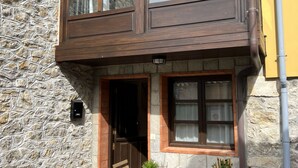 Un edificio de piedra con balcón de madera, una puerta y una ventana con cortinas.