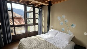 Un dormitorio con cama, ventana con cortinas, un mural floral en la pared y vistas a las montañas.