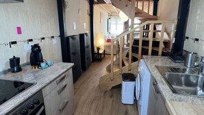 Una cocina con estufa integrada, un lavamanos y una escalera de madera que conduce a otra habitación.
