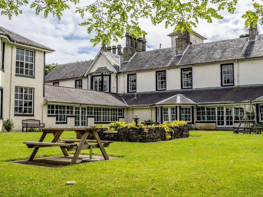 A large building with multiple windows and a lawn area with picnic tables.