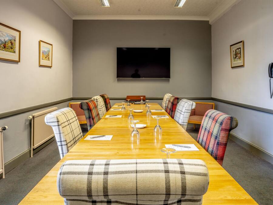 A conference room with a long table, chairs, a television, framed pictures, and a telephone.