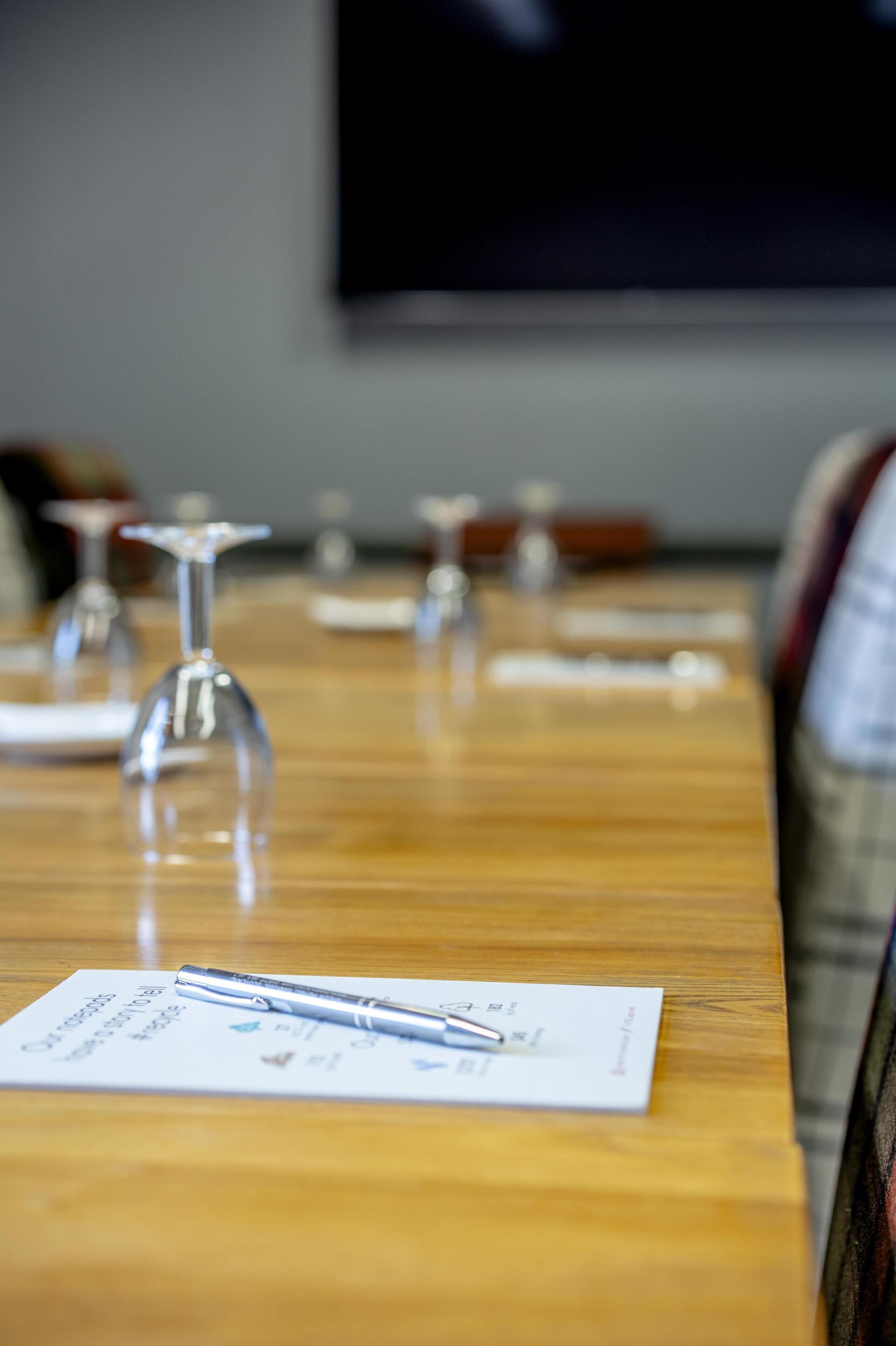 A conference table with documents and pens, a television screen in the background, and a wooden table surface.