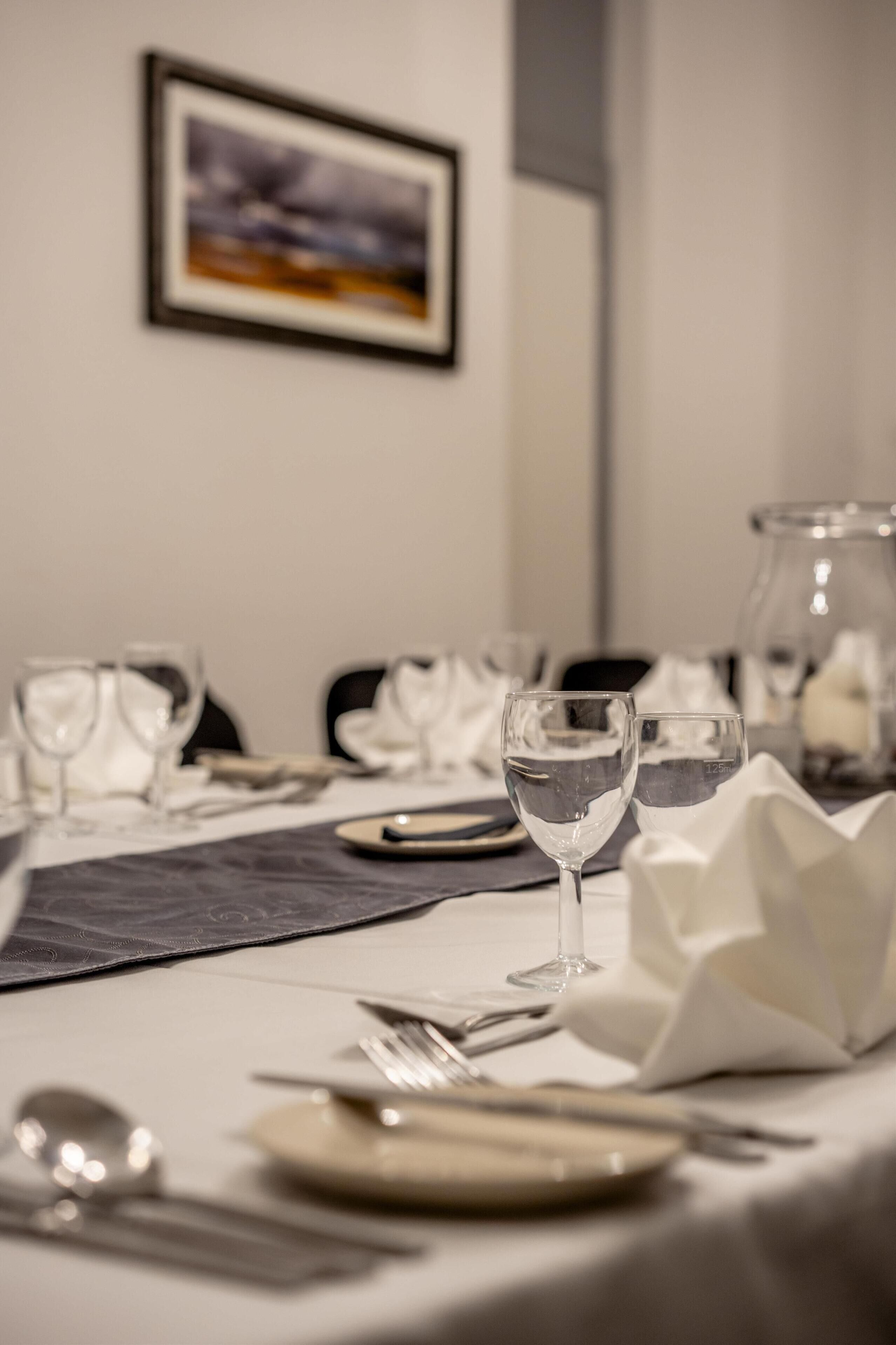 A dining table set with plates, cutlery, and wine glasses, with a framed picture on the wall.