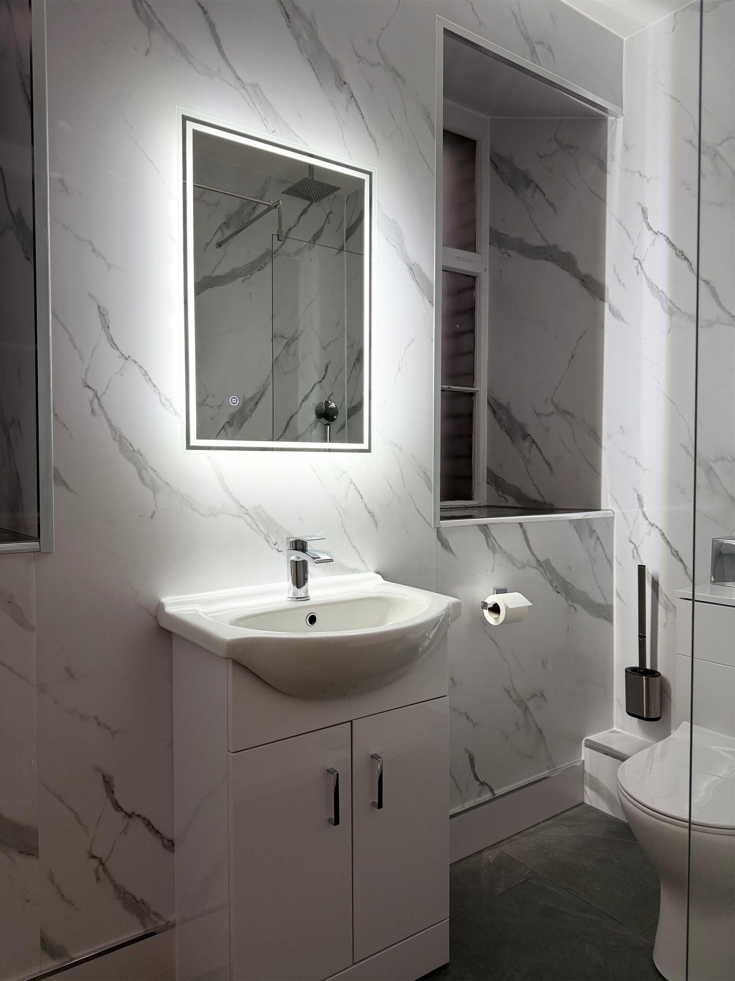 A modern bathroom with a marble backsplash, a white sink with a single faucet, a mirror above the sink, and a toilet with a bidet attachment.