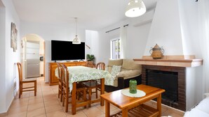 A living room with a fireplace, a television, and a dining area with wooden furniture. - Vacation Apartment in Chiclana with Pool and Garden (Chiclana de la Frontera)
