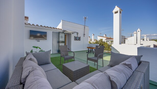 A rooftop patio with outdoor furniture, a small table, and a view of the surrounding buildings. - Vacation Apartment in Chiclana with Pool and Garden (Chiclana de la Frontera)
