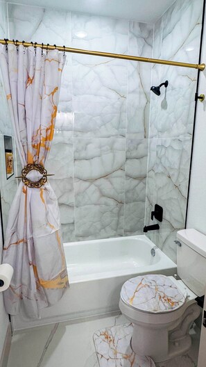 A bathroom with a marble shower wall, a bathtub, and a toilet. - Little Nyssa Home Away From Home (Houston)