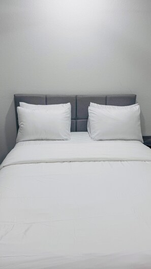 Una cama con cabecera tapizada en gris y dos almohadas blancas.