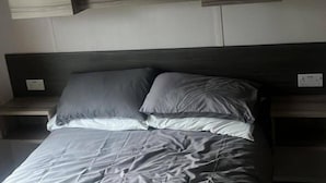 A bed with grey bedding, a dark headboard, and two bedside tables with light-colored surfaces. - Caravan- Sleeps 6, 2 Bedrooms - Thurston Manor (Dunbar)