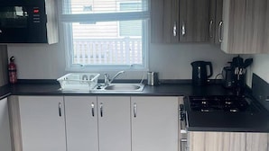 A compact kitchen with a sink, a kettle, and a stove. - Caravan- Sleeps 6, 2 Bedrooms - Thurston Manor (Dunbar)