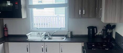 A compact kitchen with a sink, a kettle, and a stove.