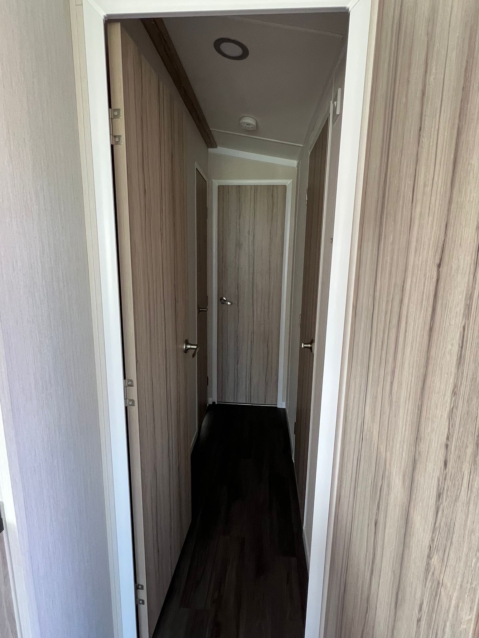 A narrow hallway with wooden doors and a dark floor.