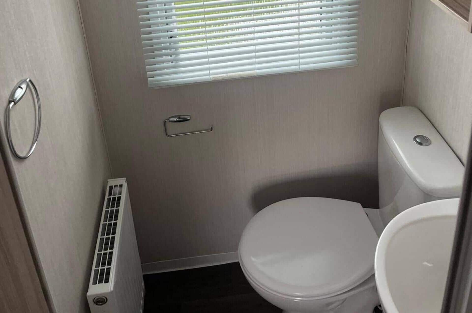 A compact bathroom with a toilet, a window with blinds, and a radiator.