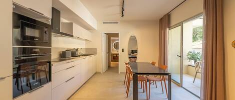 Una cocina moderna con electrodomésticos integrados, un comedor con mesa y sillas, y un ventanal corredero que da a un balcón.