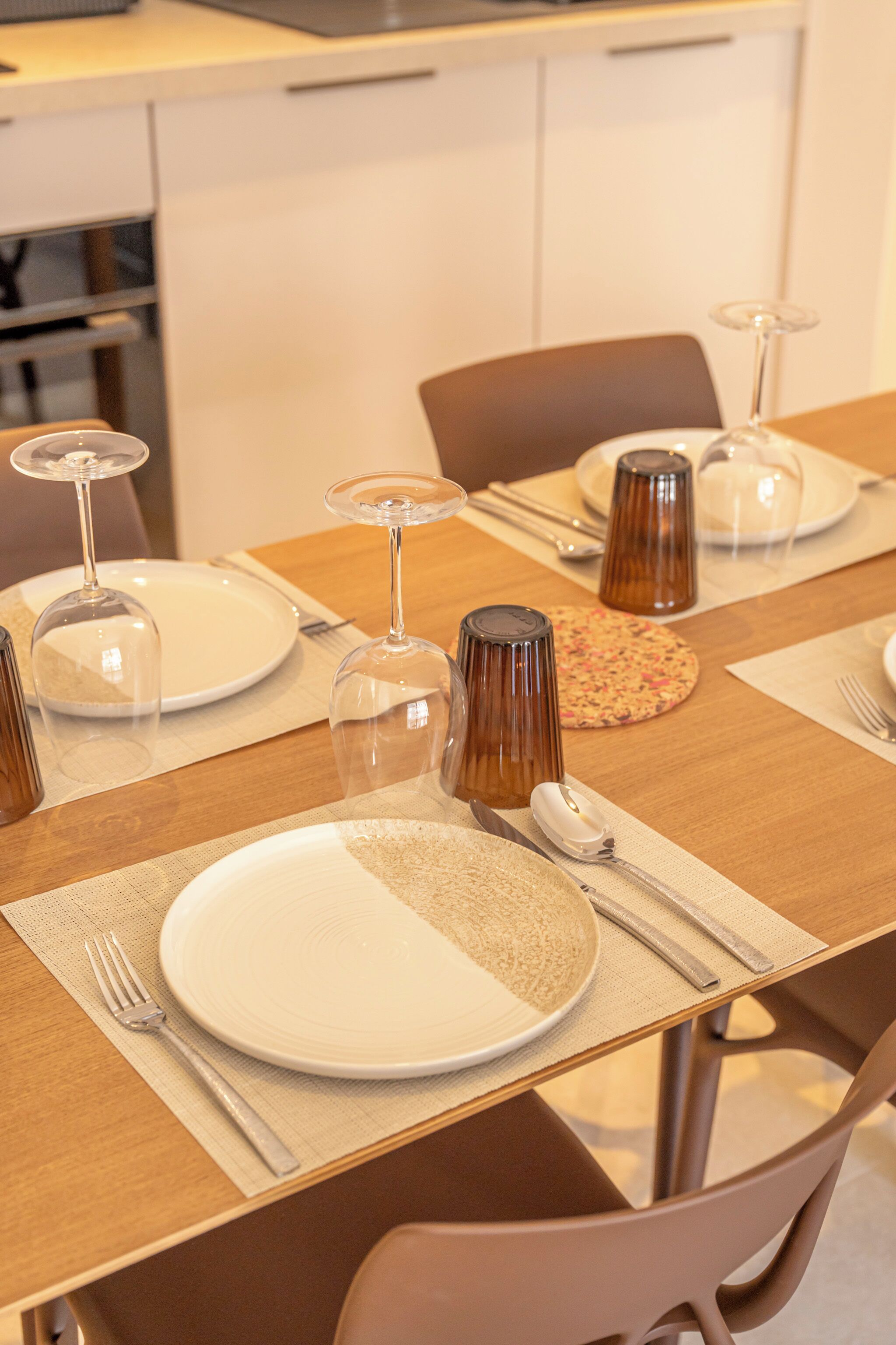 A dining table set with plates, cutlery, and wine glasses, with a chair visible in the foreground.