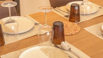Une table à manger dressée avec des assiettes, des couverts et des verres à vin, et une chaise visible au premier plan.