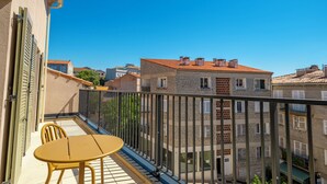 Un balcón con una mesa y sillas amarillas, con vistas a un paisaje urbano de edificios de piedra y tejados rojos.