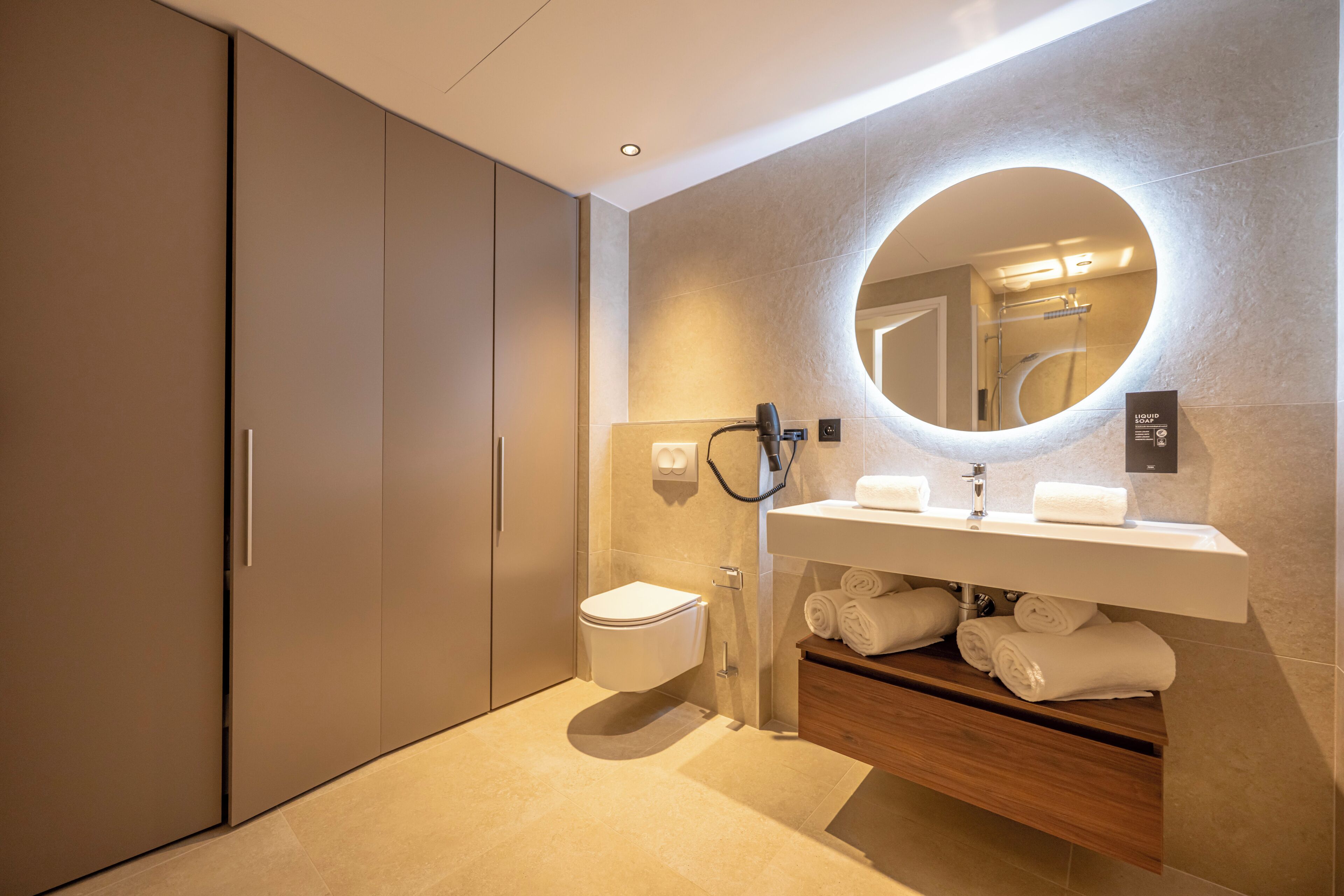 Une salle de bain moderne équipée de toilettes, d’un lavabo et d’un miroir avec un éclairage circulaire.