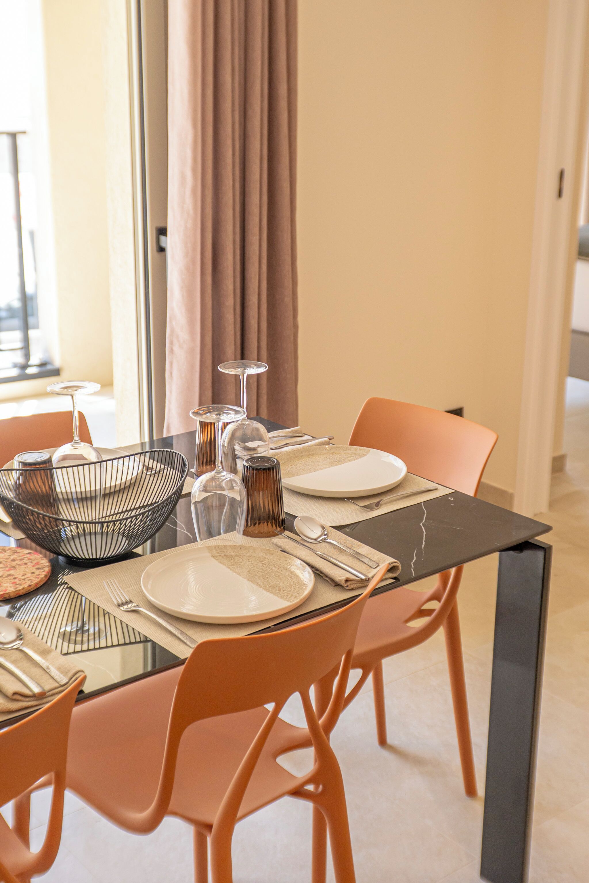 Un comedor con mesa de vidrio, sillas anaranjadas y diseño de interiores moderno.