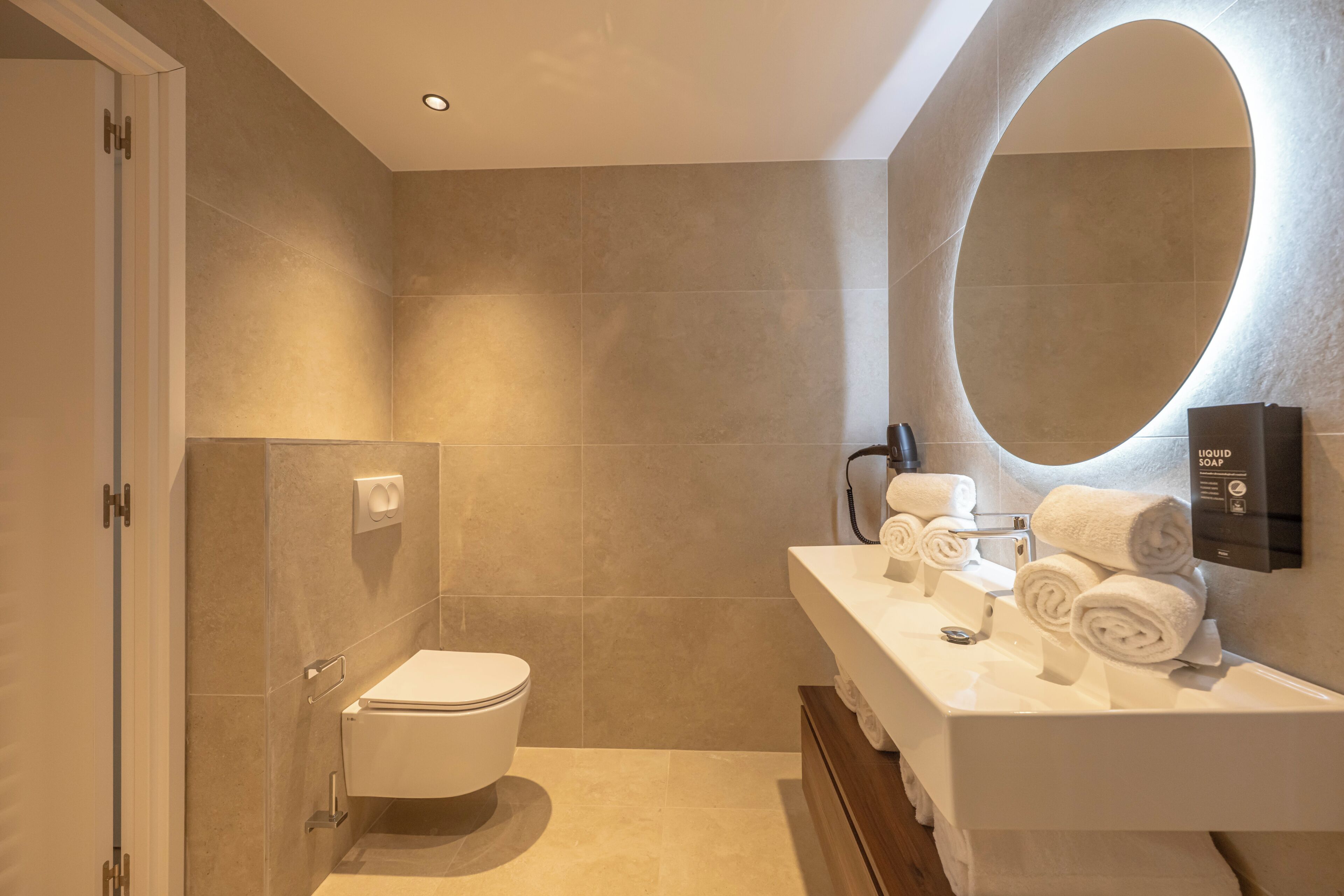 A modern bathroom with a toilet, sink, and a large mirror.
