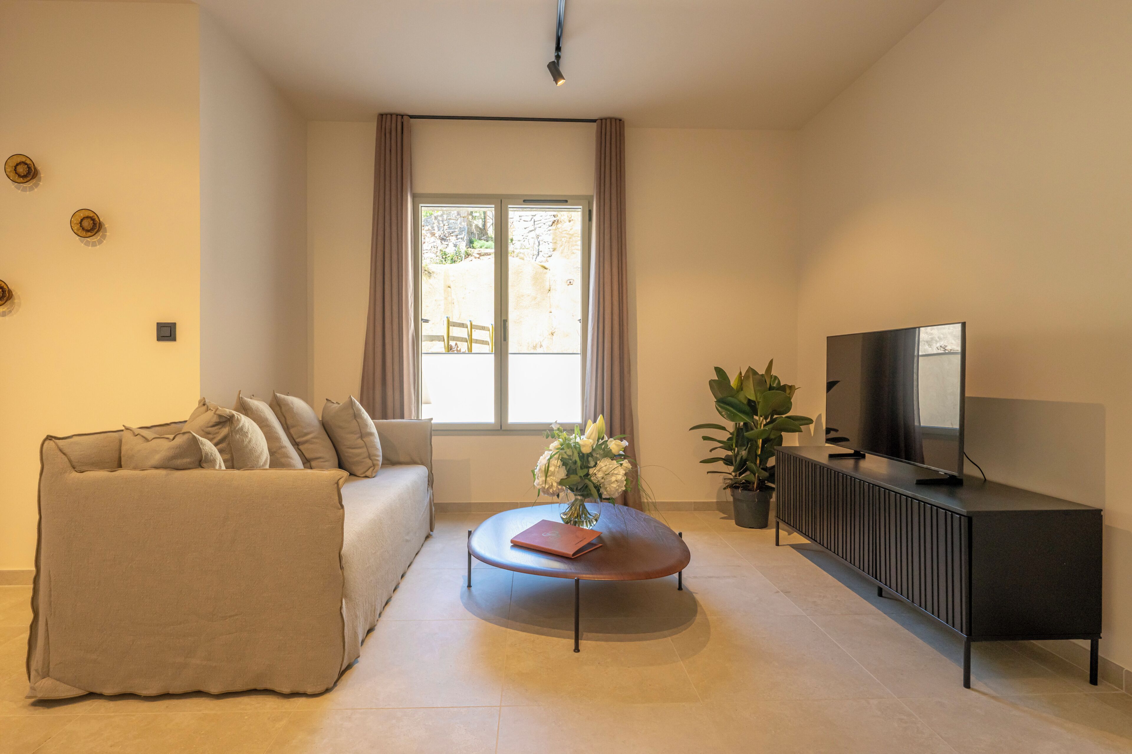 A living room with a sofa, a coffee table, a TV, and a window with curtains.
