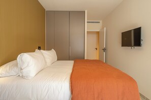 A hotel room with a bed, a wardrobe, a television, and an air conditioning unit.