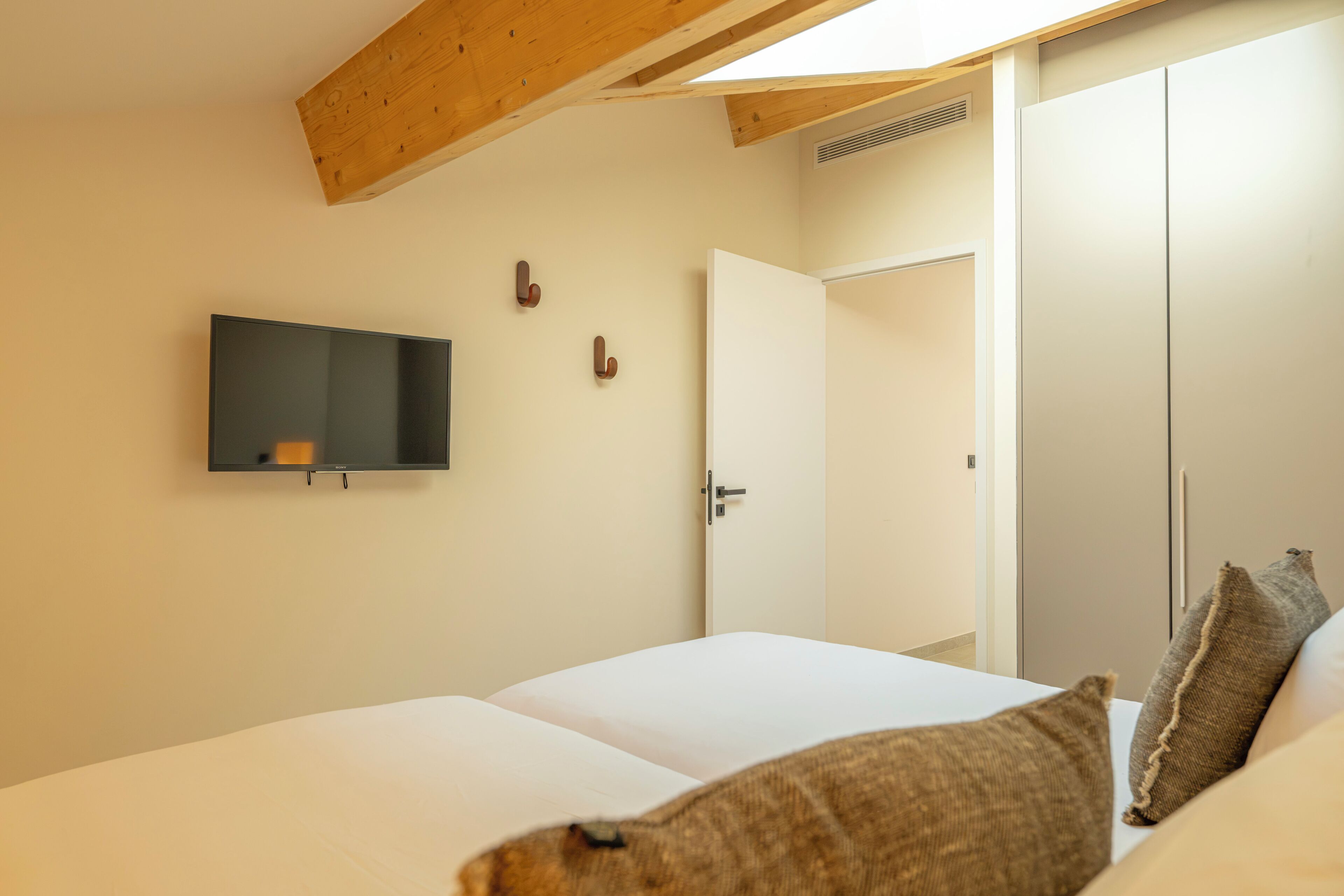 A bedroom with a bed, a television mounted on the wall, and a wardrobe.