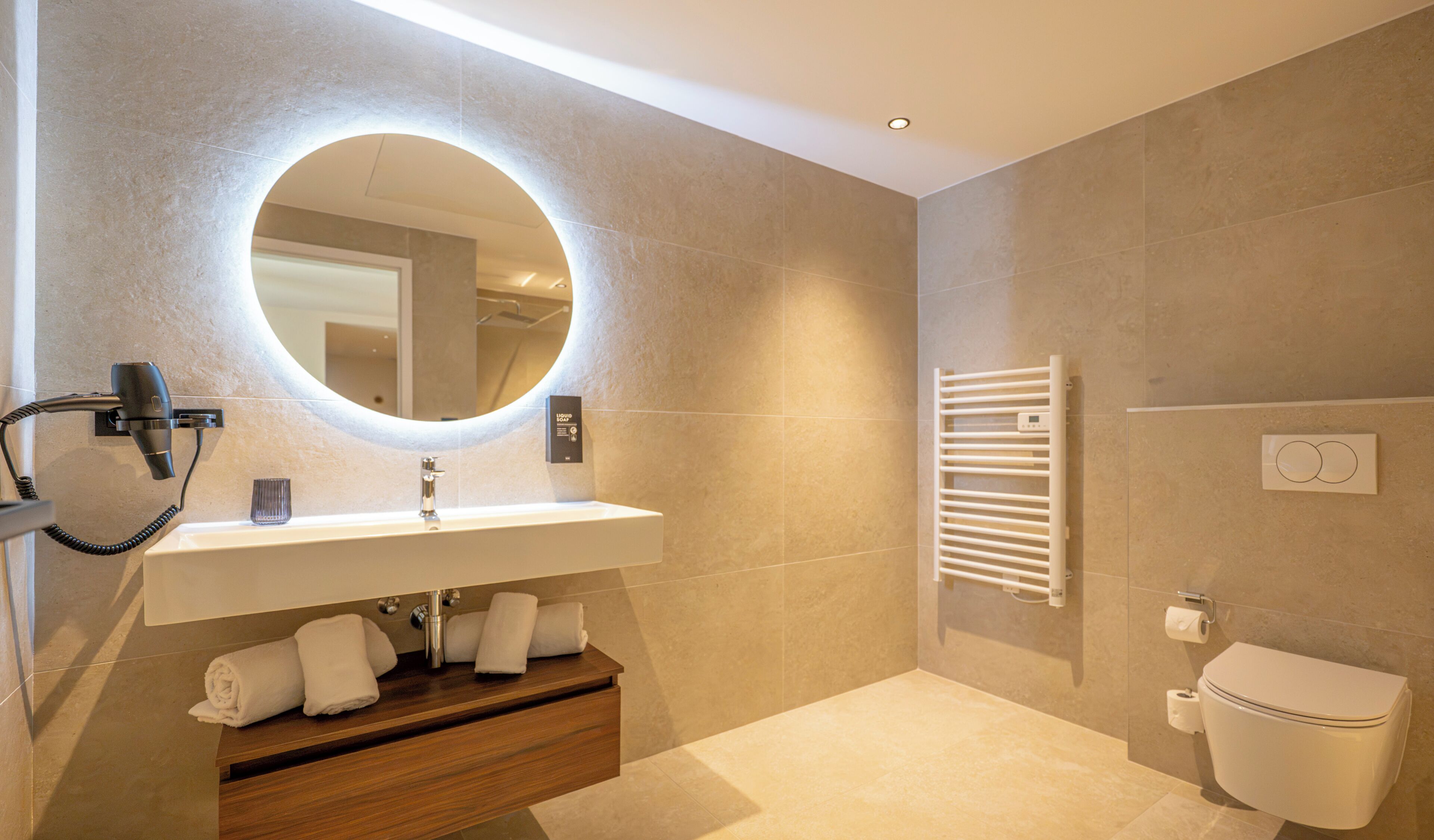 A modern bathroom with a round mirror, a built-in sink, a towel rack, a heated towel rail, and a toilet.
