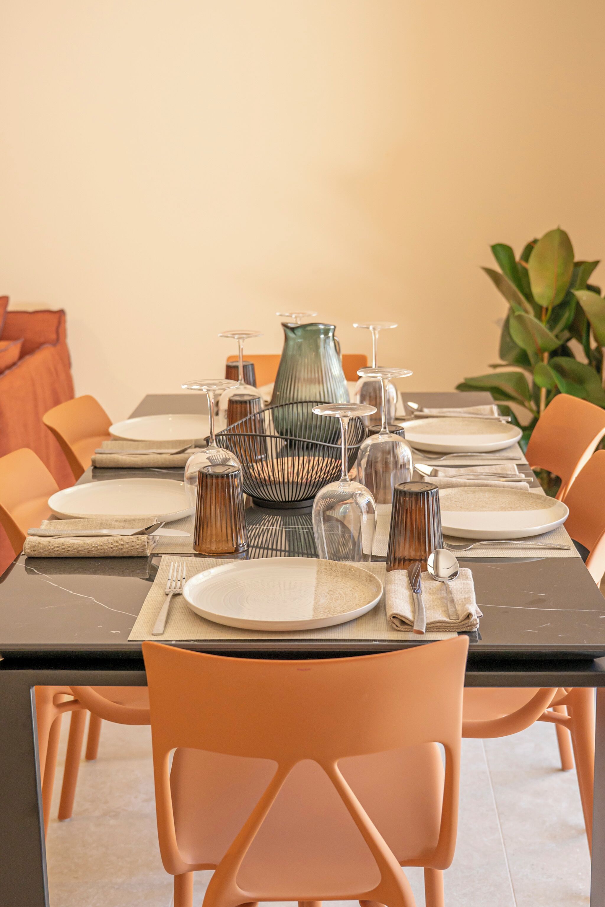A dining table set with plates, cutlery, and glassware, surrounded by orange chairs.