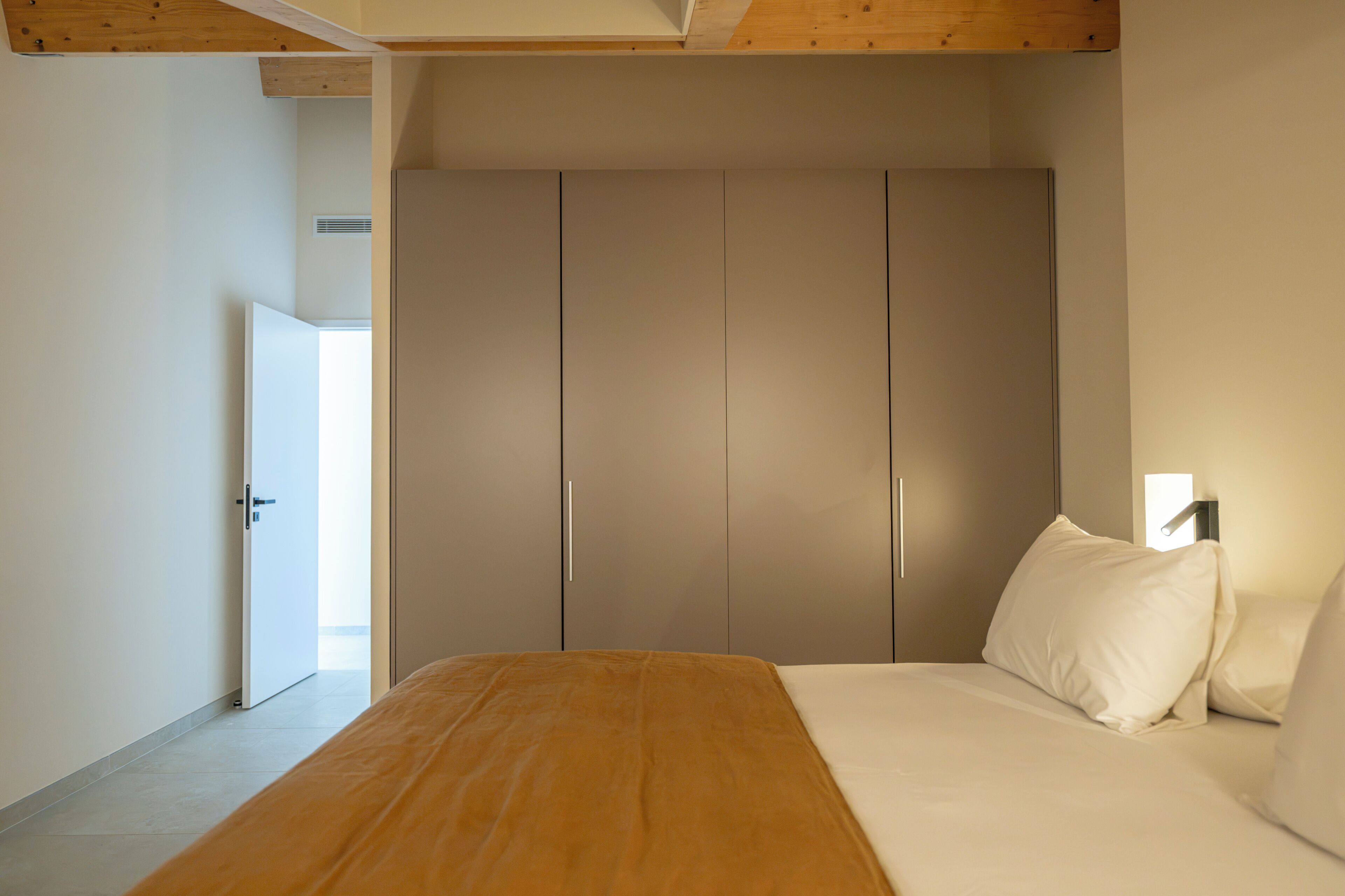 A bedroom with a bed, a wardrobe, and a door leading to another room.