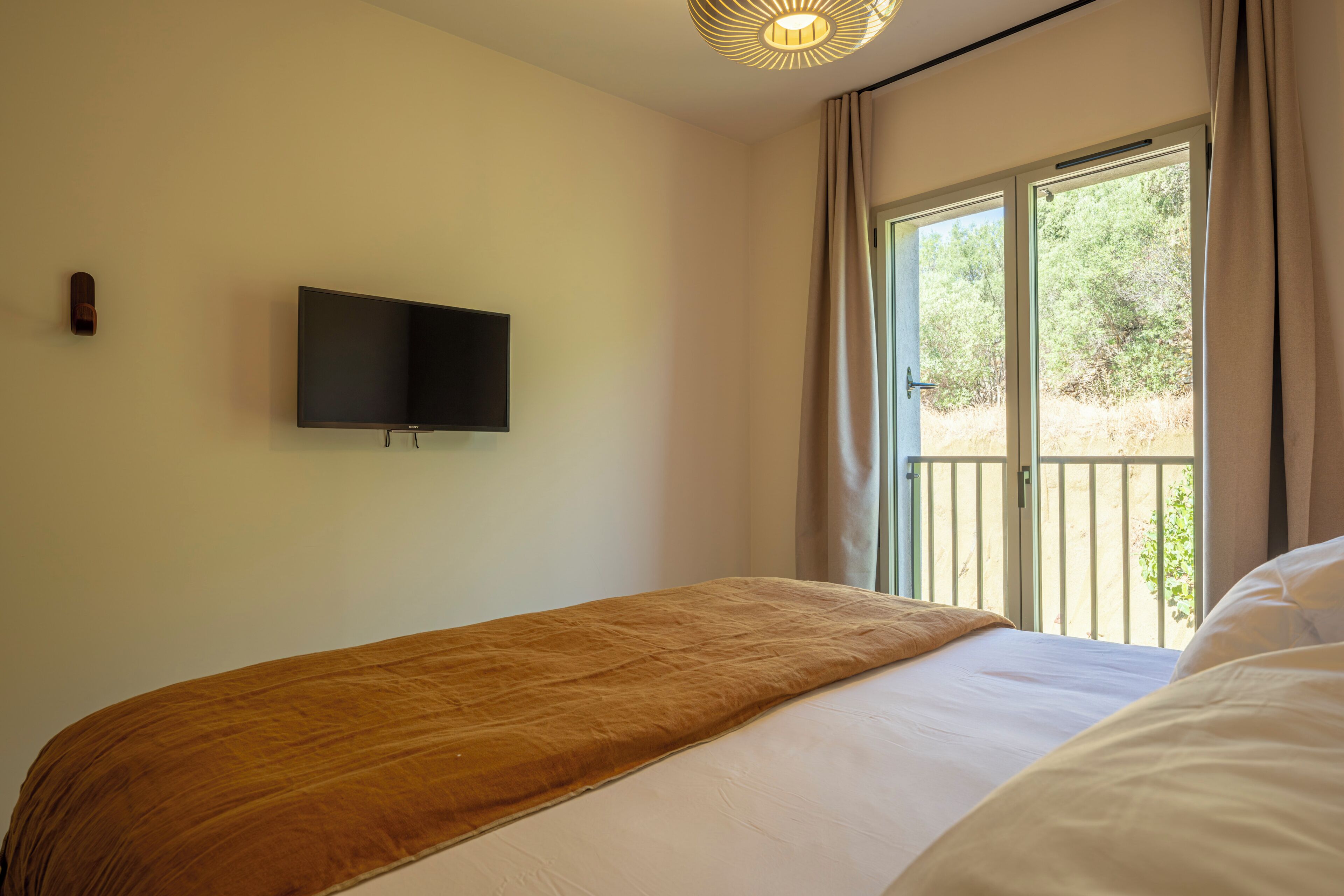 Une chambre à coucher avec un lit, un téléviseur fixé au mur et une fenêtre avec des rideaux.