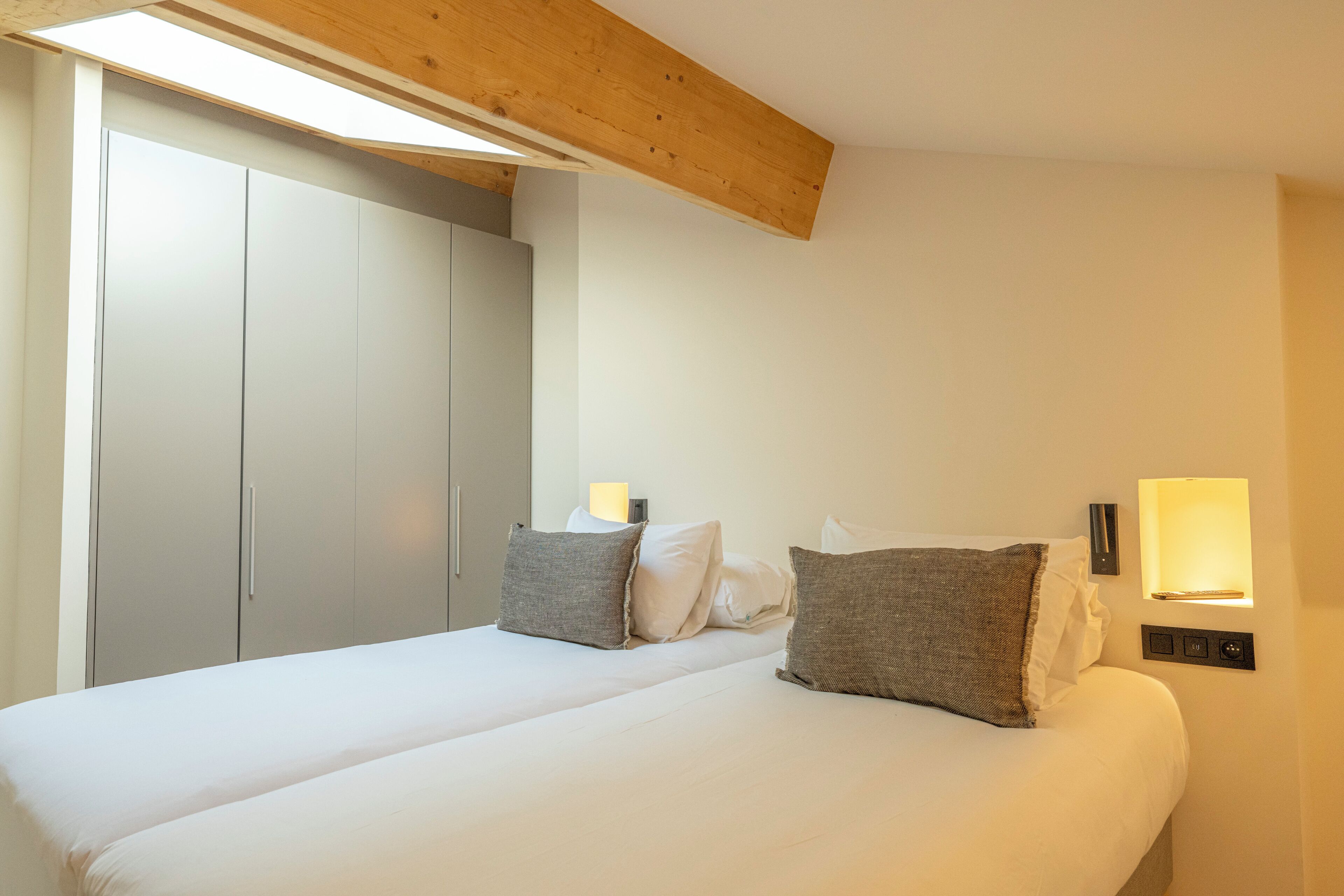 Une chambre à coucher avec un lit, des oreillers, une armoire et un luminaire fixé au mur.