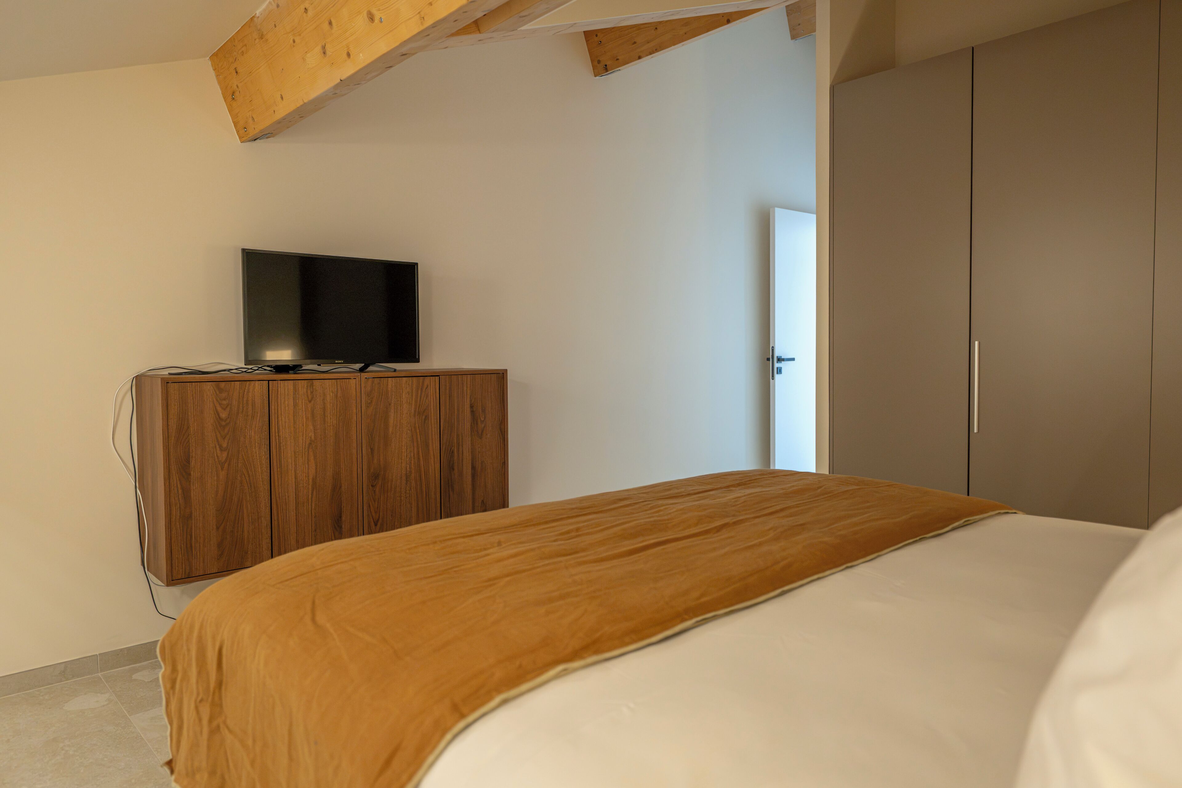 Een slaapkamer met een bed, een houten dressoir, een televisie en een kledingkast.
