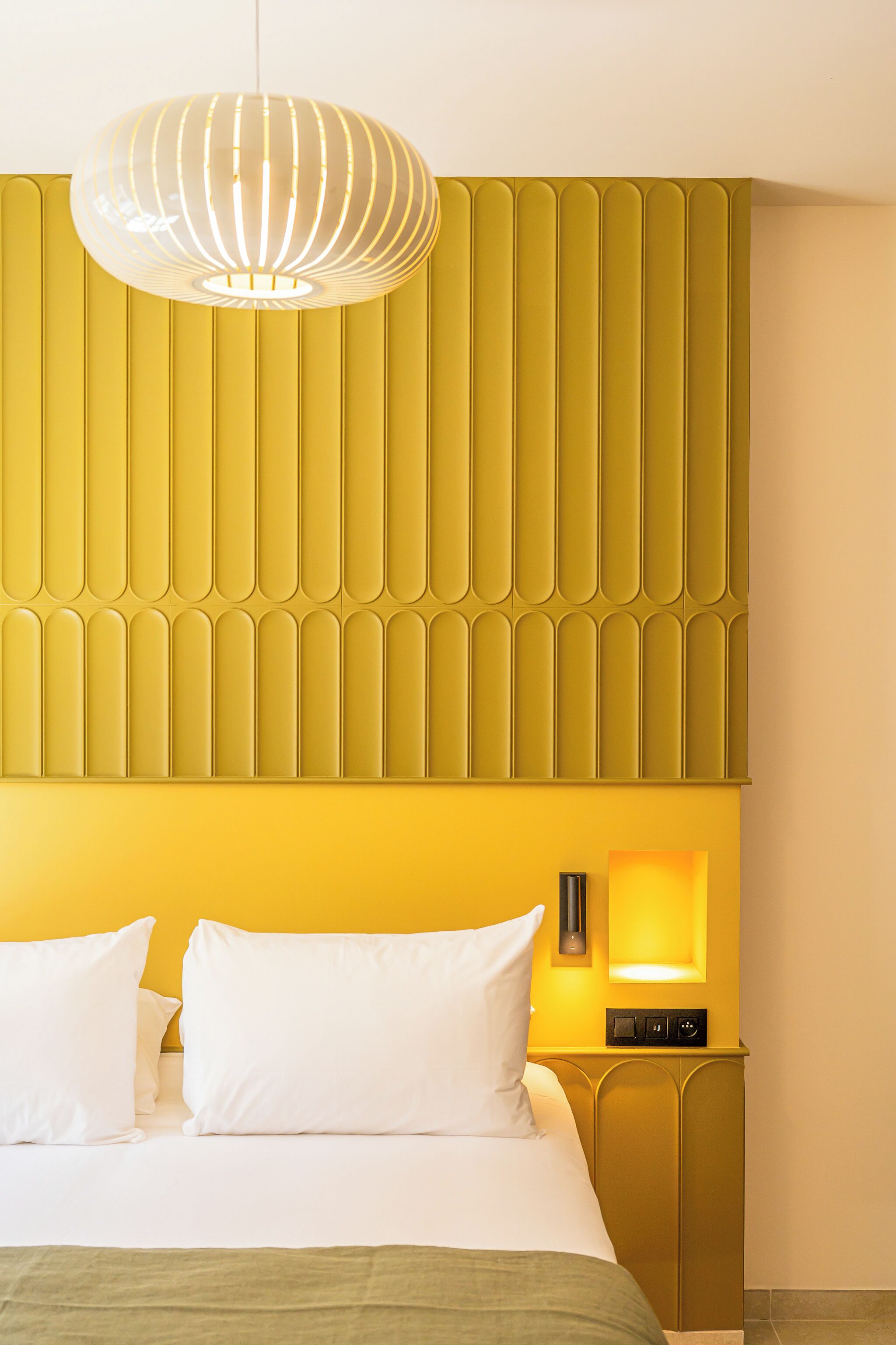Une chambre d’hôtel comprenant un lit, des oreillers, une table de chevet avec une lampe et un panneau décoratif mural.