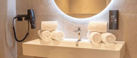 A bathroom with a round mirror, a sink, and a wooden storage unit with towels.