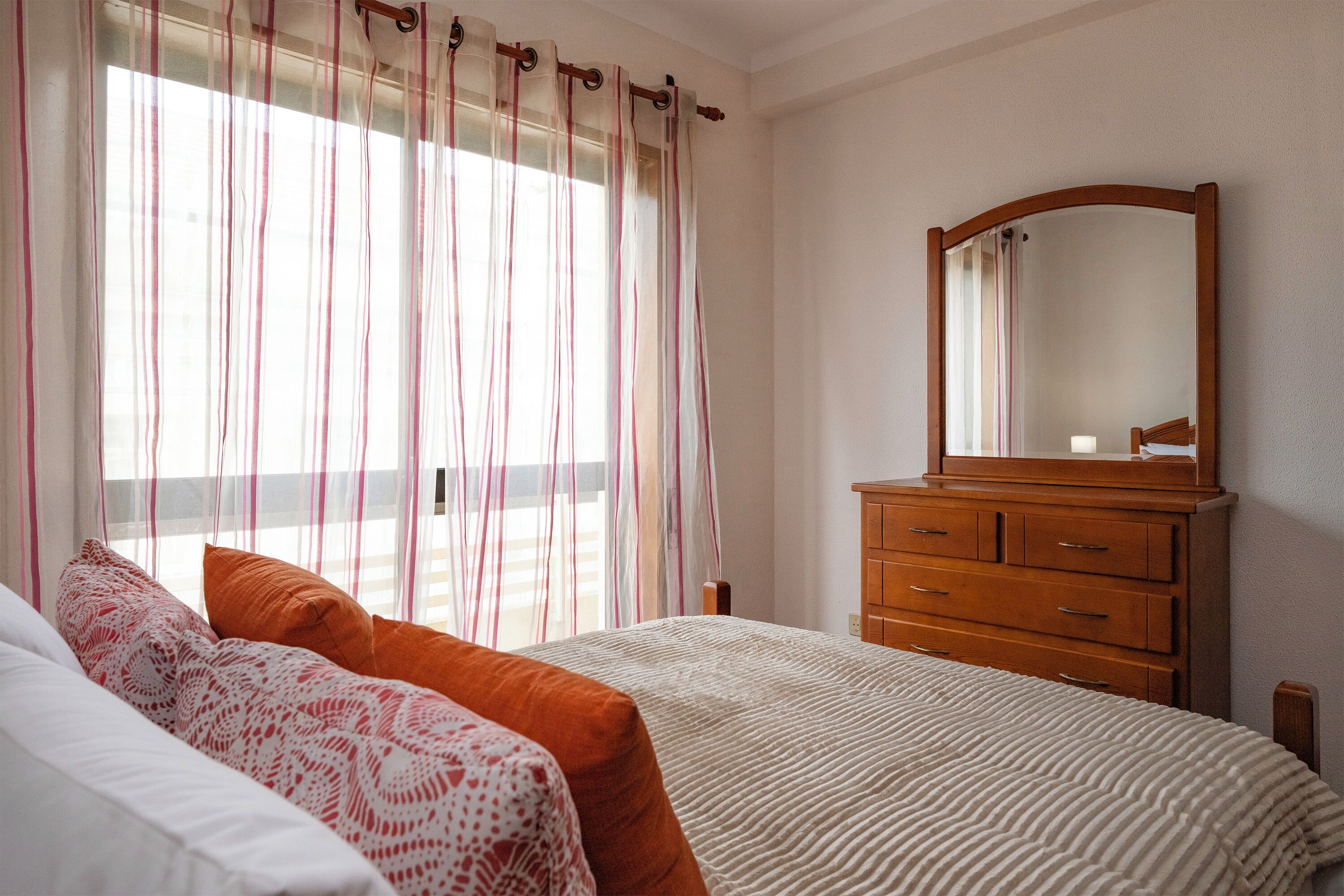 Un dormitorio con cama, cómoda y ventana con cortinas.